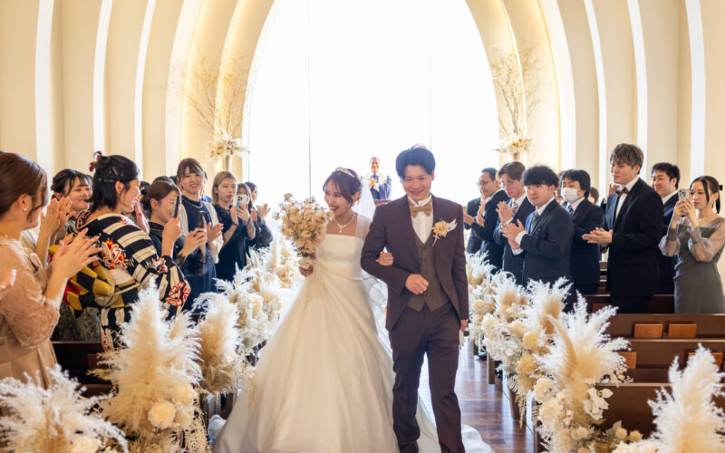 Bride and groom walk down the aisle arm in arm as guests applaud in a sunlit wedding chapel.
