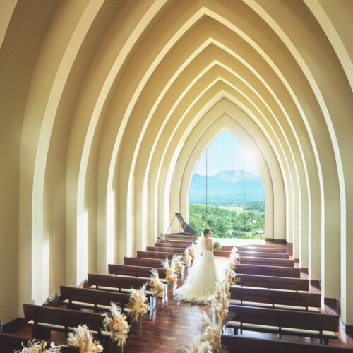 Interior of a chapel with tall arched arches leading to a window, wedding couple at the front by pews looking out to hills and mountains